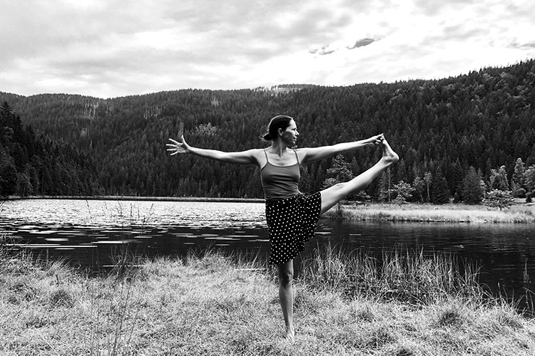 Nana Merz von Yoga Jetzt in einer Einbeinstandhaltung vor Naturkulisse am See